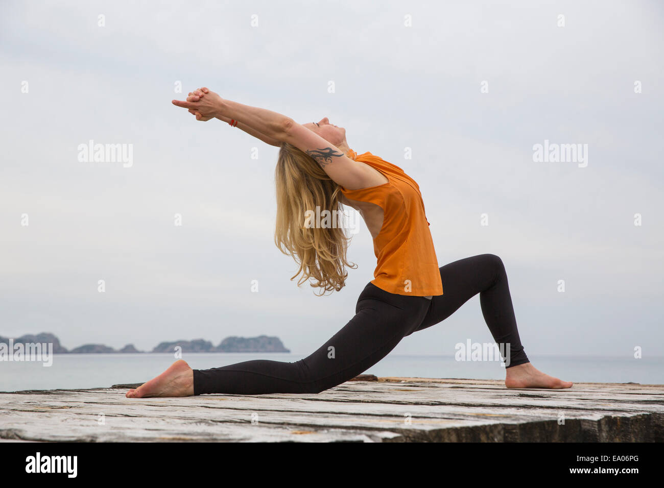 Metà donna adulta flessione all'indietro la pratica dello yoga sul mare in legno pier Foto Stock