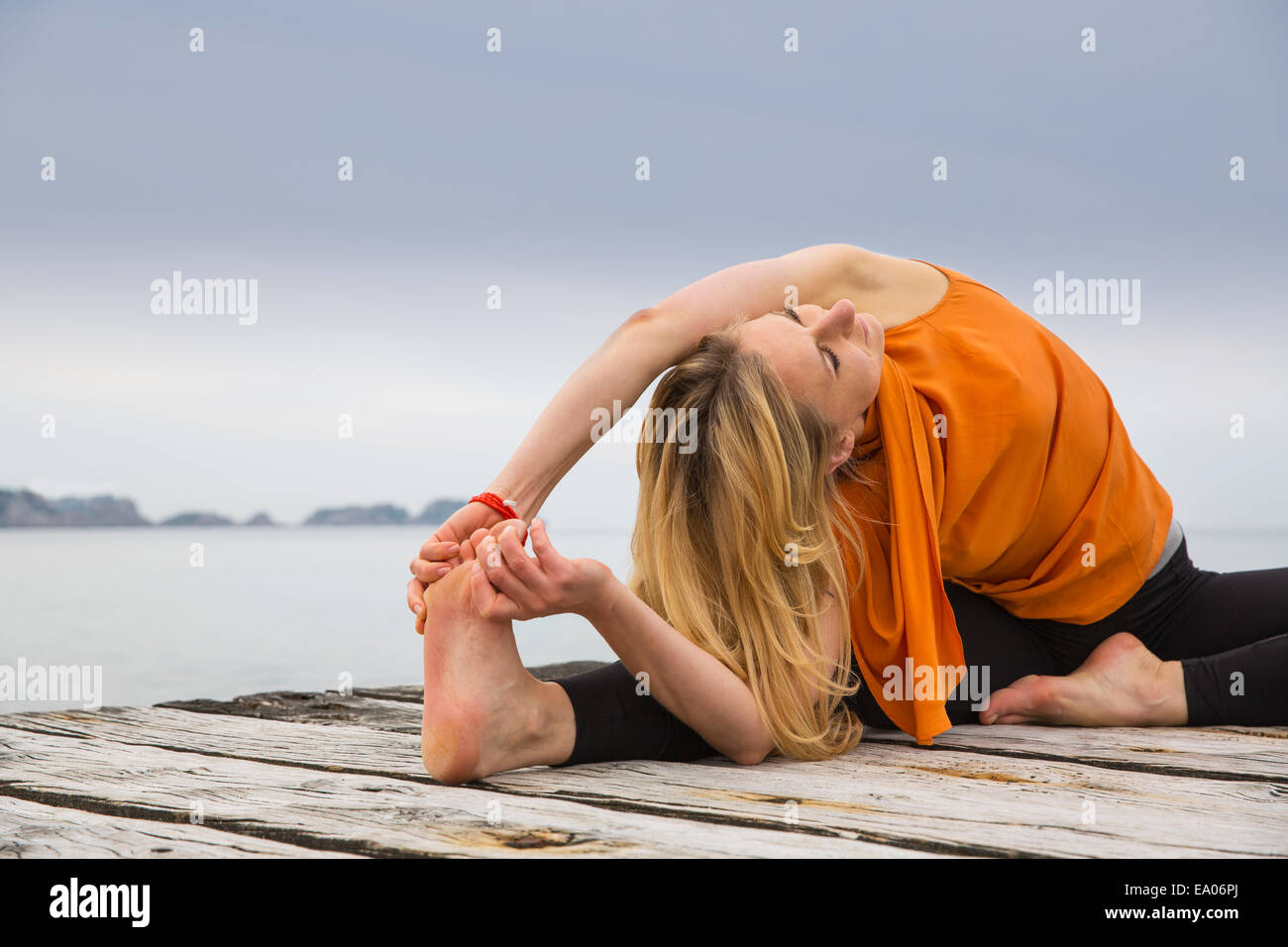 Metà donna adulta di toccare le dita dei piedi a praticare yoga sul mare in legno pier Foto Stock