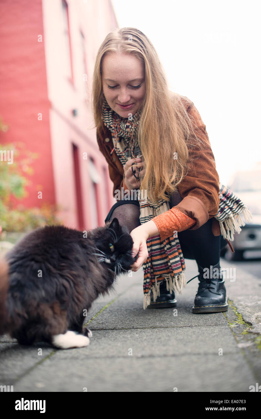 Giovane donna petting gatto nero sul marciapiede Foto Stock