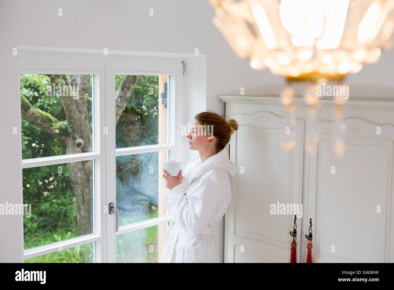 Metà donna adulta indossare accappatoio guardando fuori della finestra Foto Stock