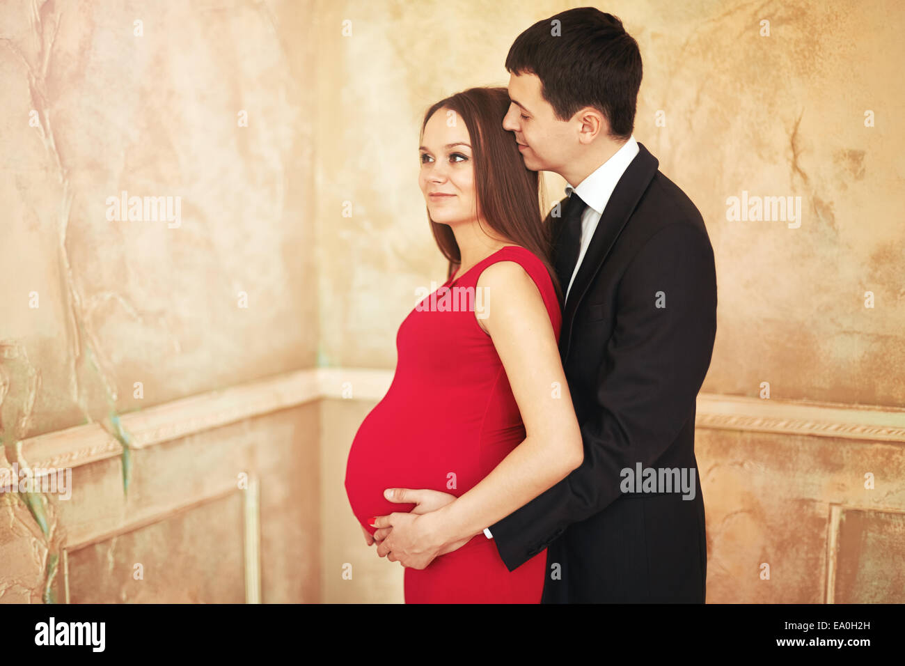 Elegante Elegante giovane coppia in attesa di un bambino. Bruna femmina rosso in abito da cocktail, uomo in smoking. Uomo Donna avvolgente. Foto Stock