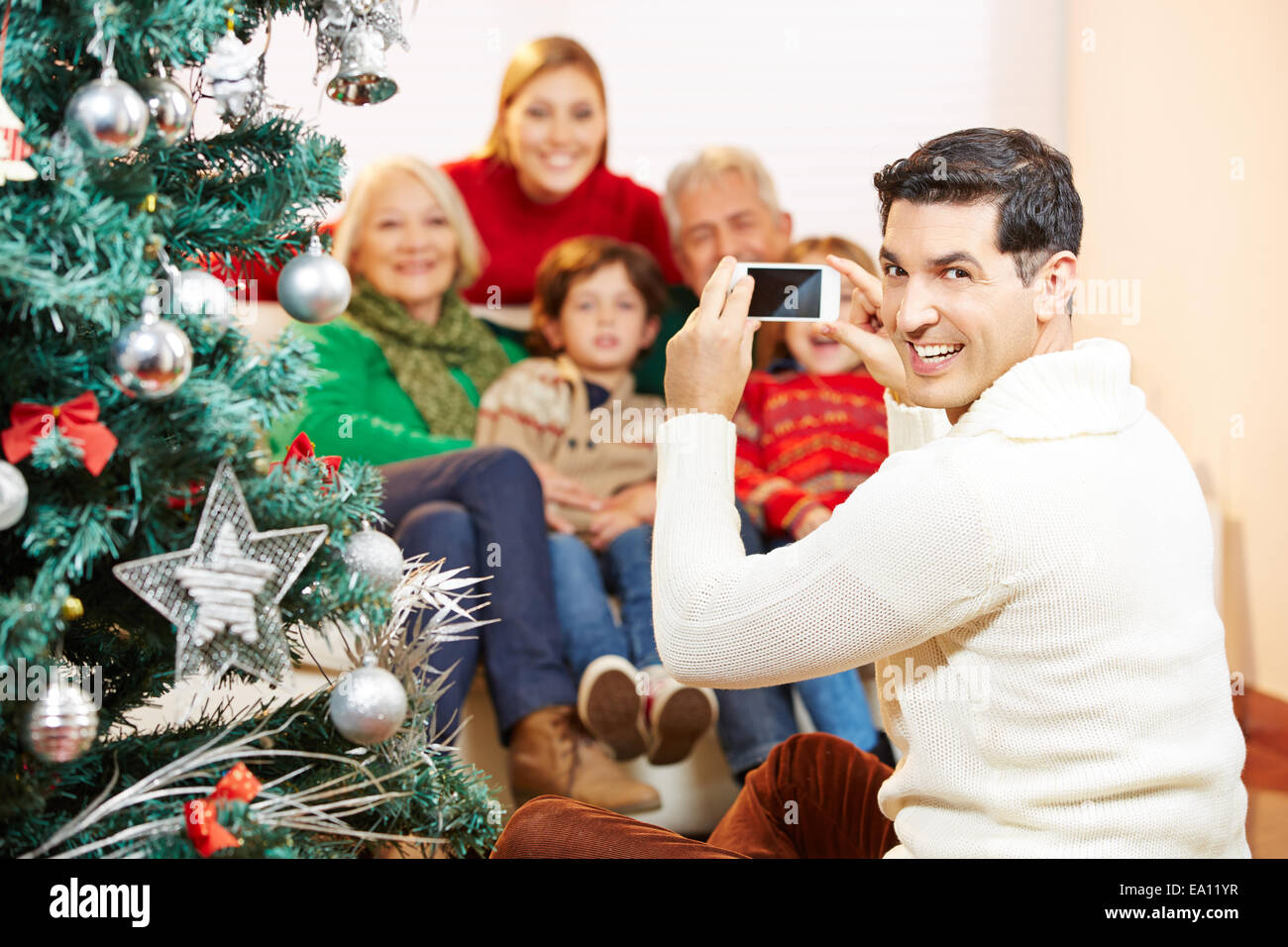 Uomo sorridente prendendo foto di famiglia in occasione del Natale con la sua fotocamera dello smartphone Foto Stock