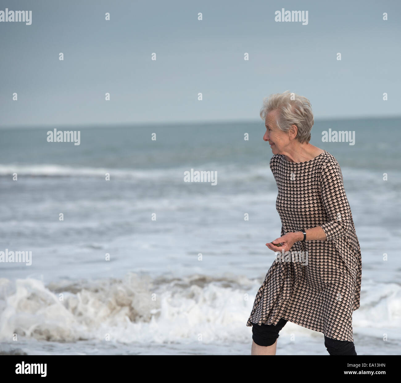 Senior donna in esecuzione dall'oceano onda sulla spiaggia, Dana Point, California, Stati Uniti d'America Foto Stock