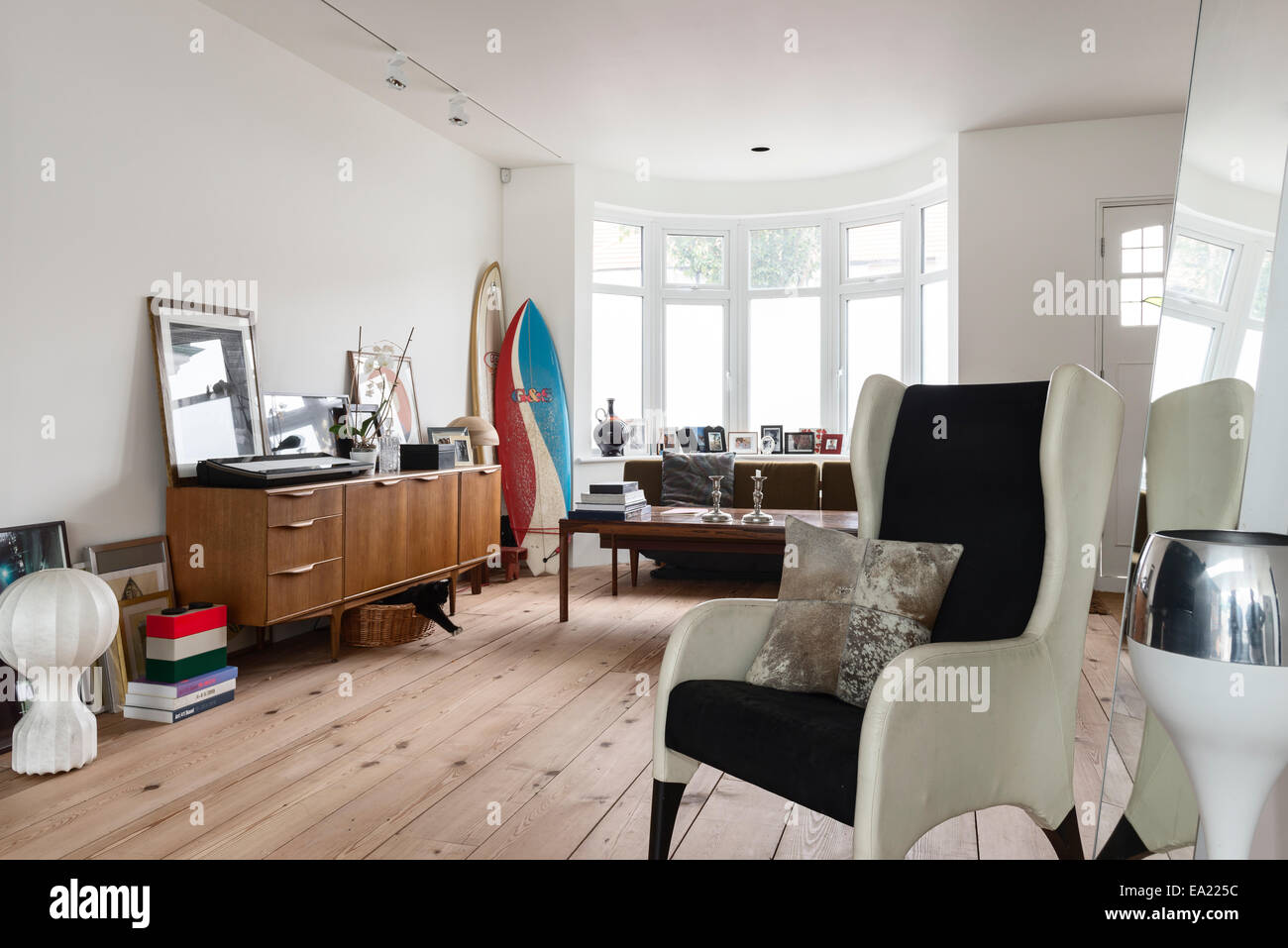 Moderne poltrone wingback in luminoso arioso spazio soggiorno con pavimento in legno e tavole da surf in angolo Foto Stock