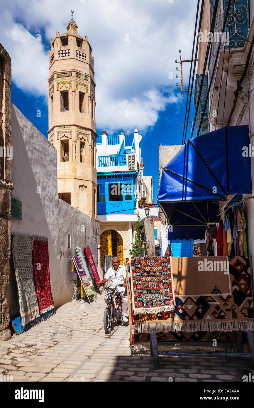 L'uomo cavalca un ciclomotore strada verso il basso con il minareto ottagonale del Zaouia Zakkak in background nella Medina di Sousse,Tunisia Foto Stock