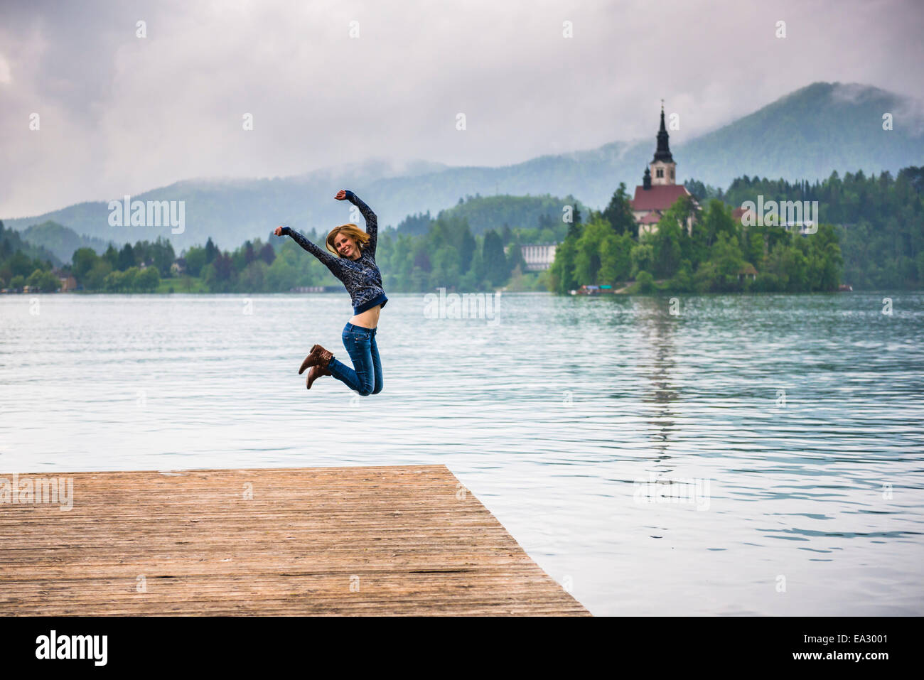 Donna salti di gioia e il lago di Bled e sulle Alpi Giulie, Gorenjska, Slovenia, Europa Foto Stock