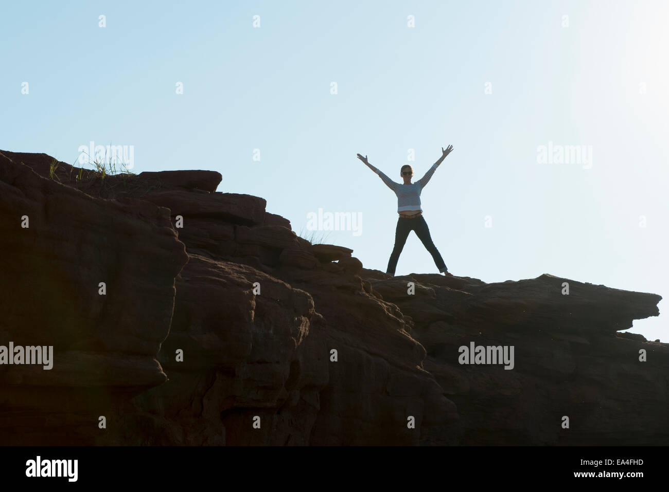 Una donna si erge su una sporgenza di roccia con le braccia sollevate nella celebrazione; Prince Edward Island, Canada Foto Stock
