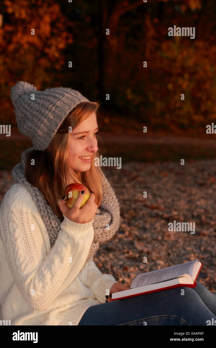 Felice ragazza seduta con libro e apple sul tramonto, verticale Foto Stock