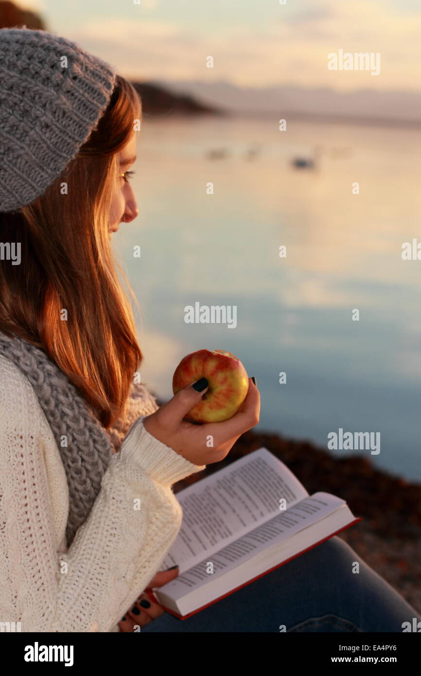 Felice ragazza seduta con libro e apple sul tramonto Foto Stock