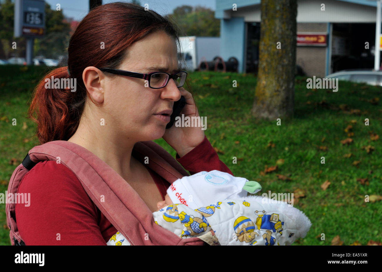Una madre che porta un bambino e utilizzando un telefono cellulare Foto Stock