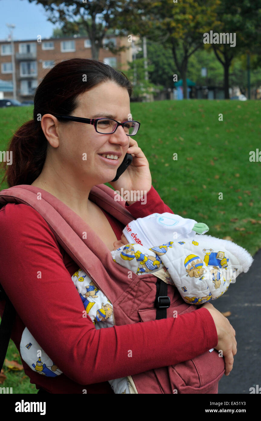 Una madre che porta un bambino e utilizzando un telefono cellulare Foto Stock