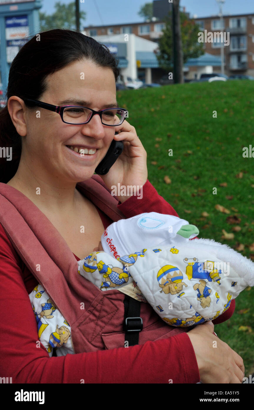 Un ridere madre che porta un bambino e utilizzando un telefono cellulare Foto Stock