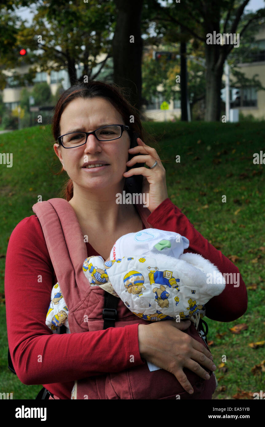 Una madre che porta un bambino e utilizzando un telefono cellulare Foto Stock