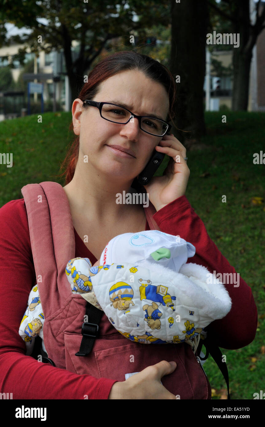 Una madre che porta un bambino e utilizzando un telefono cellulare Foto Stock