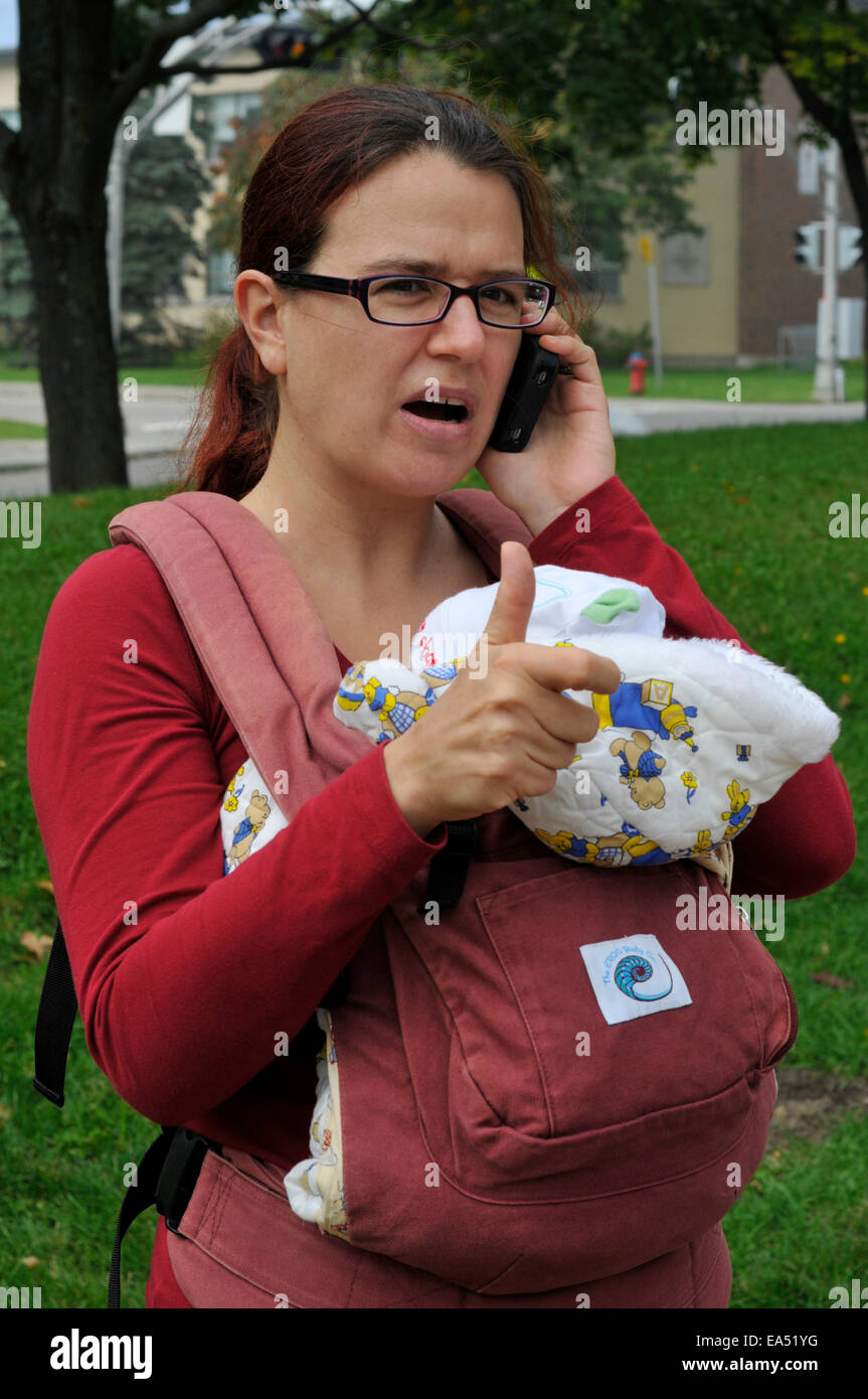 Una madre che porta un bambino e gesticulating utilizzando un telefono cellulare Foto Stock