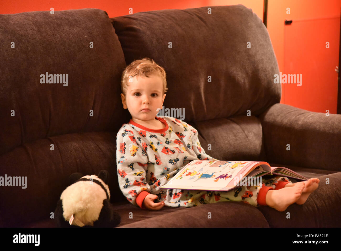 Un giovane ragazzo (due e una metà di anni) in pigiama seduto su un divano a leggere un libro appena prima di andare a dormire Foto Stock