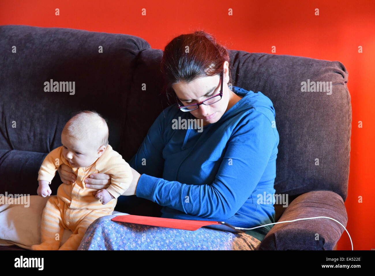 Una madre in pigiama utilizzando un ipad e ignorando la sua Gridando bambino Foto Stock