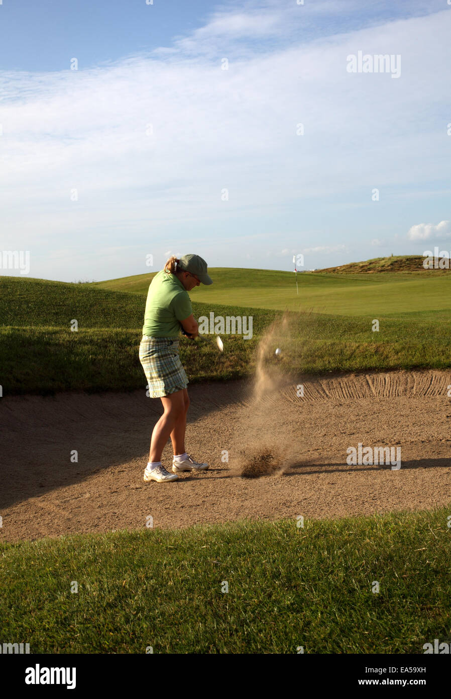 Un professional golfer donna di colpire la sua palla fuori di un bunker con la sabbia e la sfera a mezz aria Foto Stock