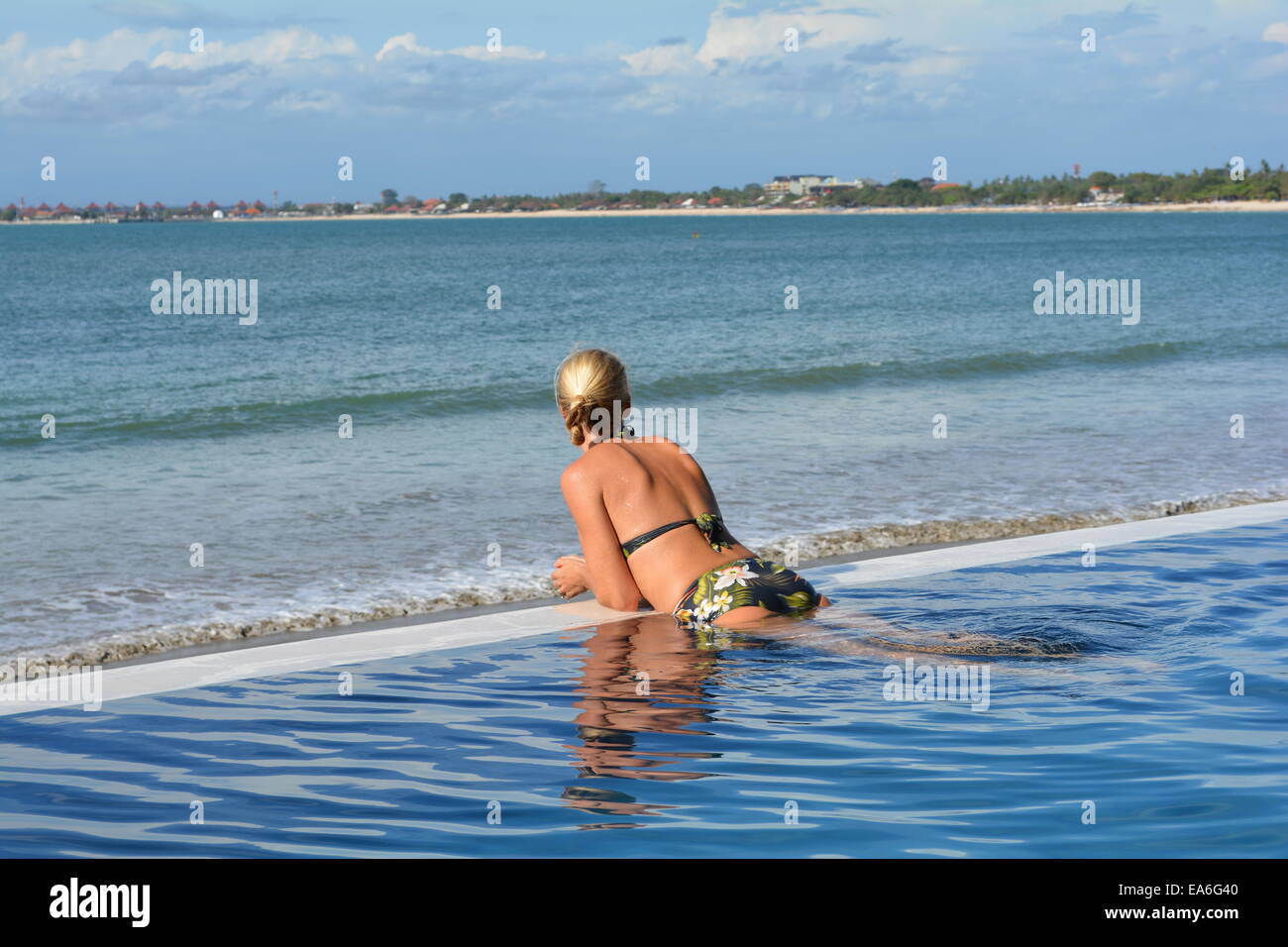 Vista posteriore della donna appoggiata sul bordo della piscina in spiaggia Foto Stock
