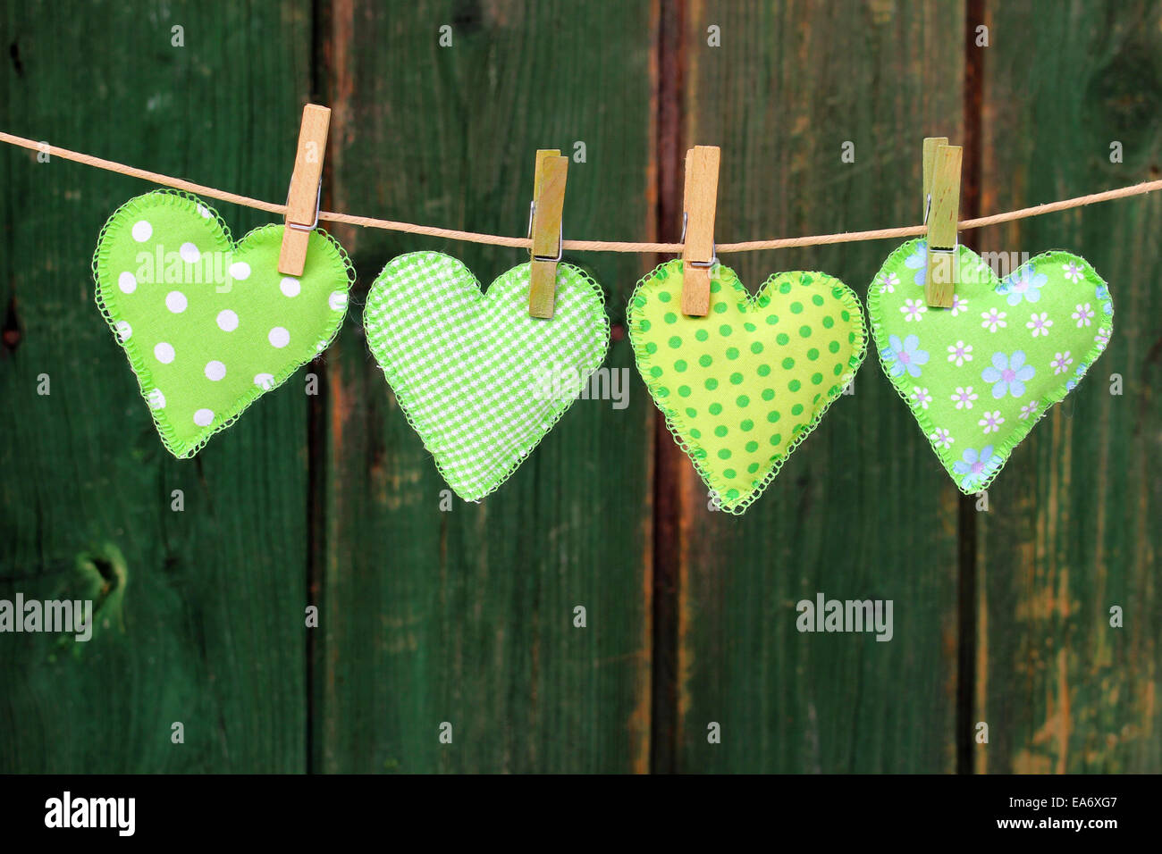 Varie cucito a mano il cuore verde di tela appeso al guinzaglio davanti a sfondo di legno Foto Stock