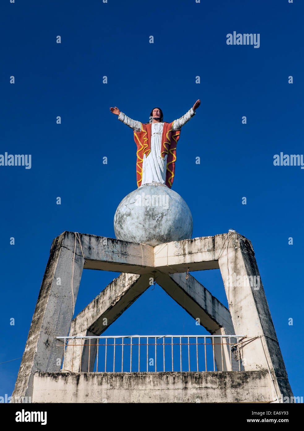 Una statua di cemento di Gesù Cristo si erge sulla cima di un globo di calcestruzzo sulla cima di una torre nella chiesa cantiere in Dimiao, Bohol, Filippine Foto Stock