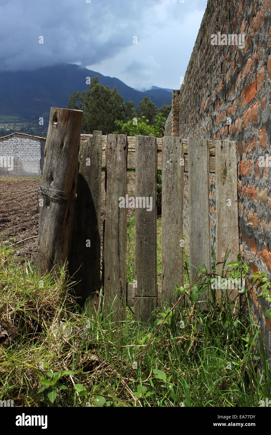 Un cancello di legno accanto a un muro di mattoni di adobe in Cotacachi, Ecuador Foto Stock