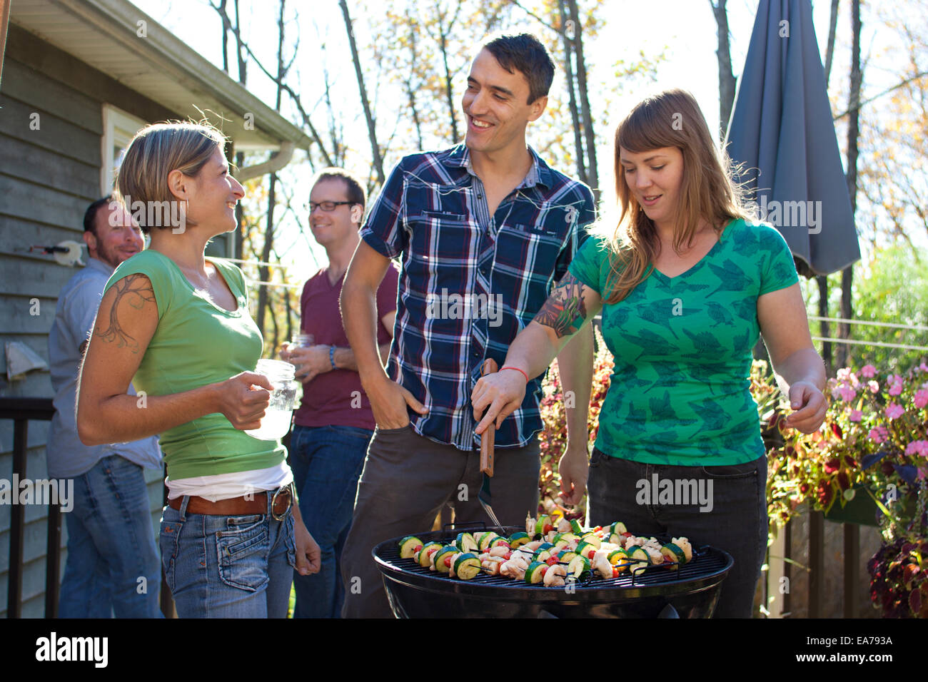 Cinque persone in piedi dal grill barbecue nel cortile posteriore Foto Stock