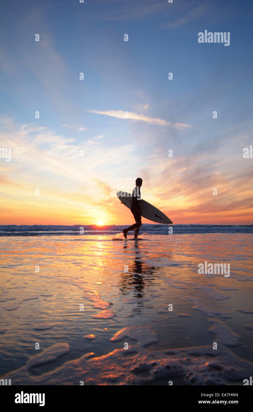 Basso angolo vista del surfista con la tavola da surf a piedi lungo il bordo delle acque durante il tramonto Constantine Bay vicino a Padstow North Cornwall Sout Foto Stock