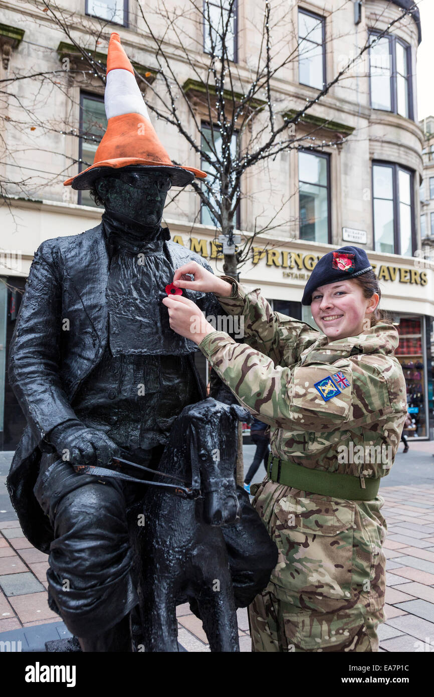 Glasgow, Scotland, Regno Unito. 8 Novembre, 2014. Abby Malcolm, 16 anni, da Maryhill, Glasgow, Scozia, un membro del segnale reale cadetti, la raccolta di semi di papavero in Scozia a Buchanan Street, Glasgow. Qui, lei ripone un papavero su Kevin Powell, da Cheshire, una strada intrattenitore e "statua vivente' chi è in costume che imita la statua del ben noto statua del generale Arthur Wellesley, primo duca di Wellington, in Royal Exchange Square, iconically visto con un cono di parcheggio sulla sua testa. Credito: Findlay/Alamy Live News Foto Stock