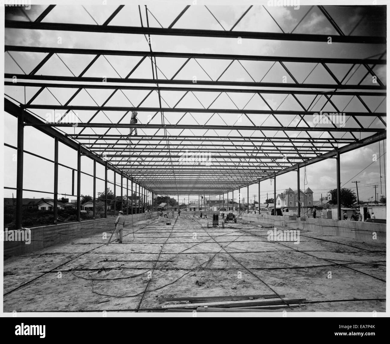 Questa immagine raffigura la costruzione di un magazzino, che mostra i processi architettonici e industriali necessari per la creazione di una grande struttura commerciale. Mette in evidenza i materiali, i lavoratori e le tecniche di costruzione utilizzate. Foto Stock