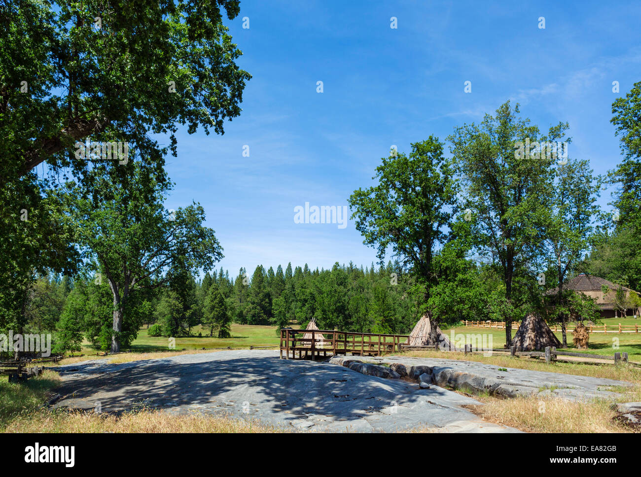 La macinazione di roccia con Miwok corteccia case dietro, macinazione indiano Rock State Historic Park, Southern Gold Country, CALIFORNIA, STATI UNITI D'AMERICA Foto Stock