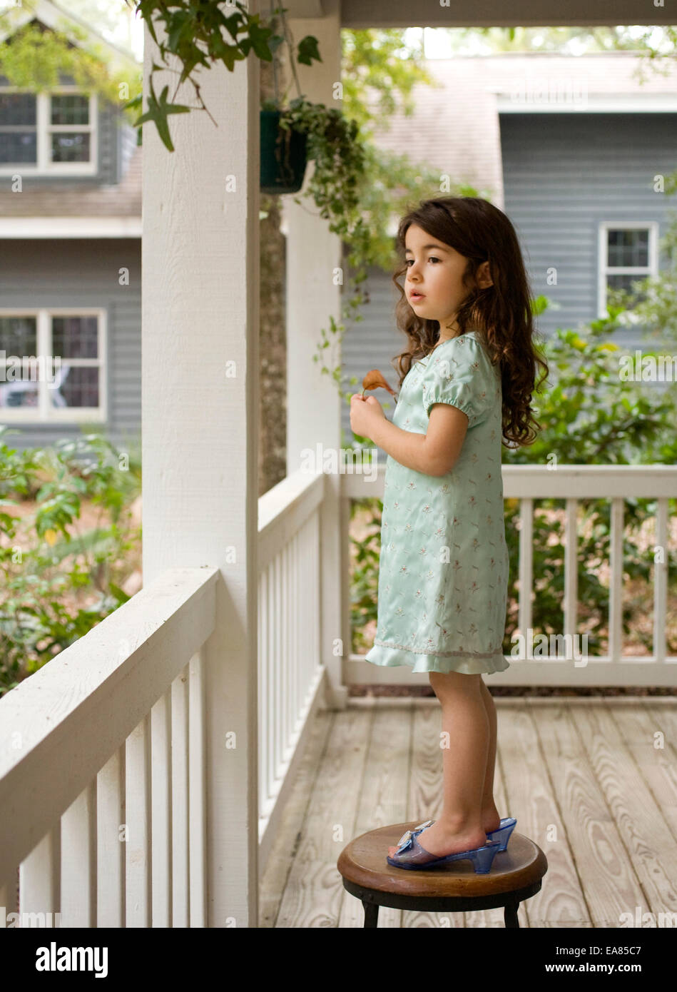 Giovane ragazza in gioco le scarpe in piedi su uno sgabello sul portico Foto Stock