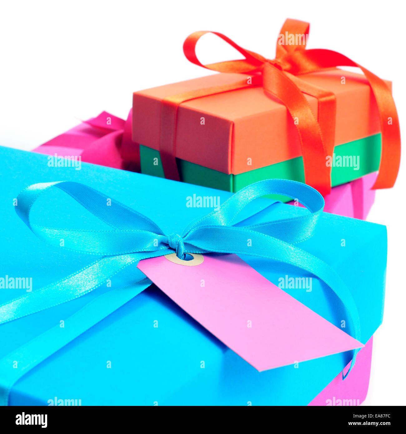 Primo piano di una pila di confezioni regalo di diversi colori legata con nastri di raso di colori diversi con un'etichetta vuota su un bianco ba Foto Stock