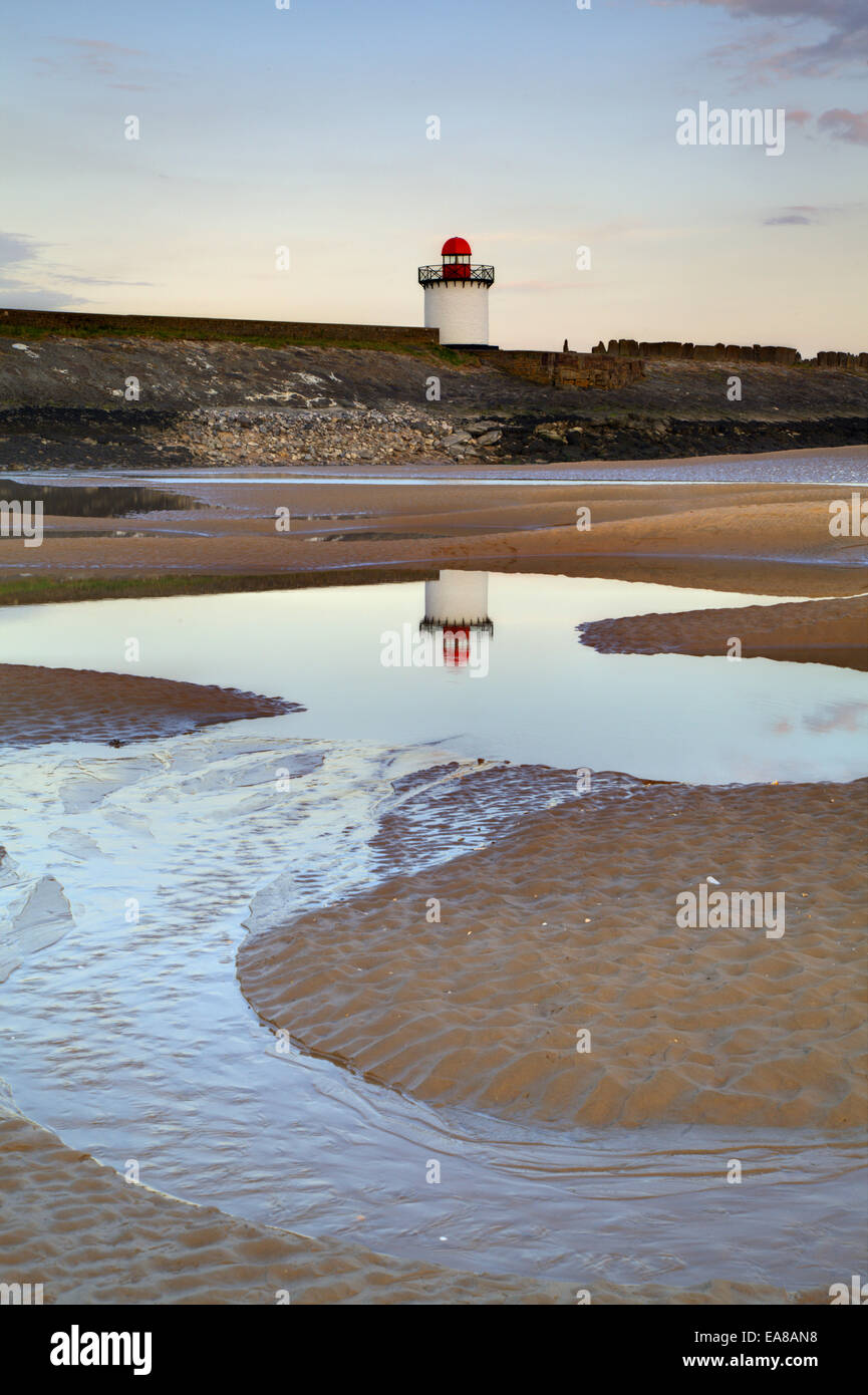 Burry Port faro al crepuscolo. Preso in formato verticale con il faro che riflette in una pozza nella spiaggia di sabbia. Foto Stock