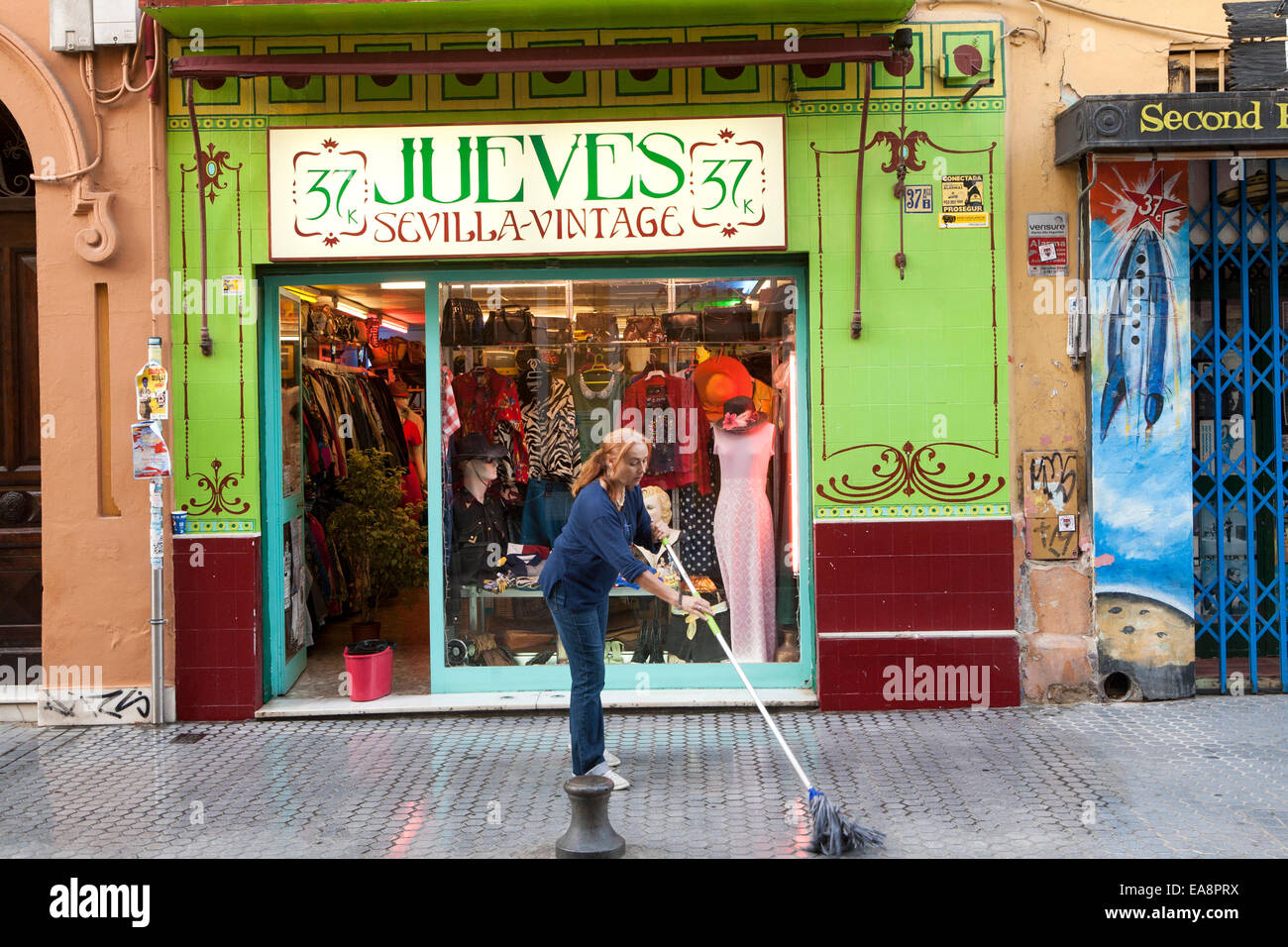 Donna con straccio la strada fuori Jueves vintage negozio di abbigliamento in Barrio Macarena, Siviglia, Spagna Foto Stock