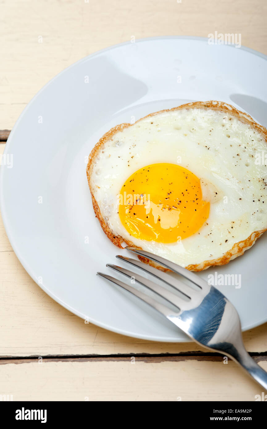 Uovo fritto soleggiato lato su una piastra con la forcella sulla tavola di legno Foto Stock