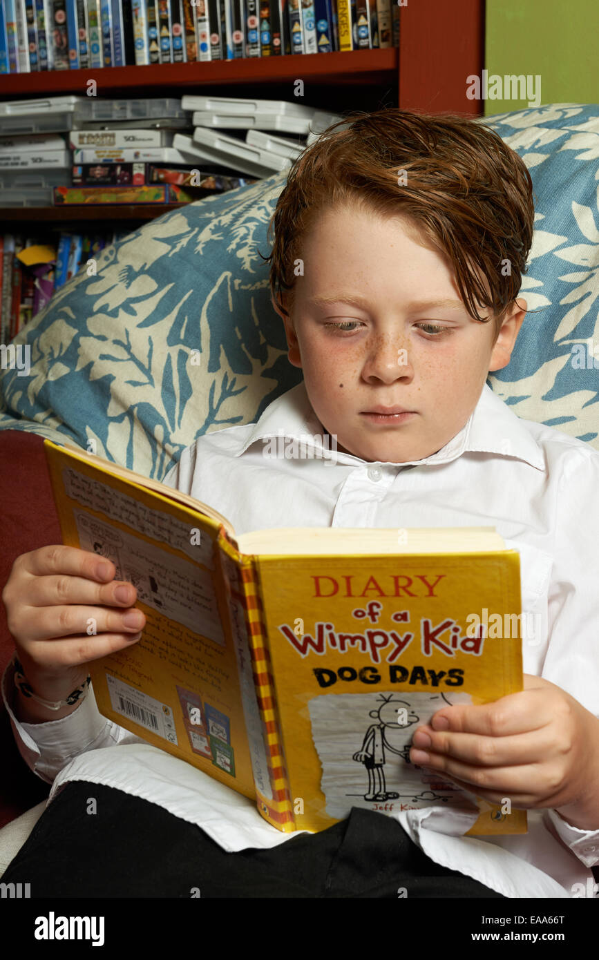 Schoolboy a casa leggendo Diario di un Wimpy Kid Dog Days libro Foto Stock