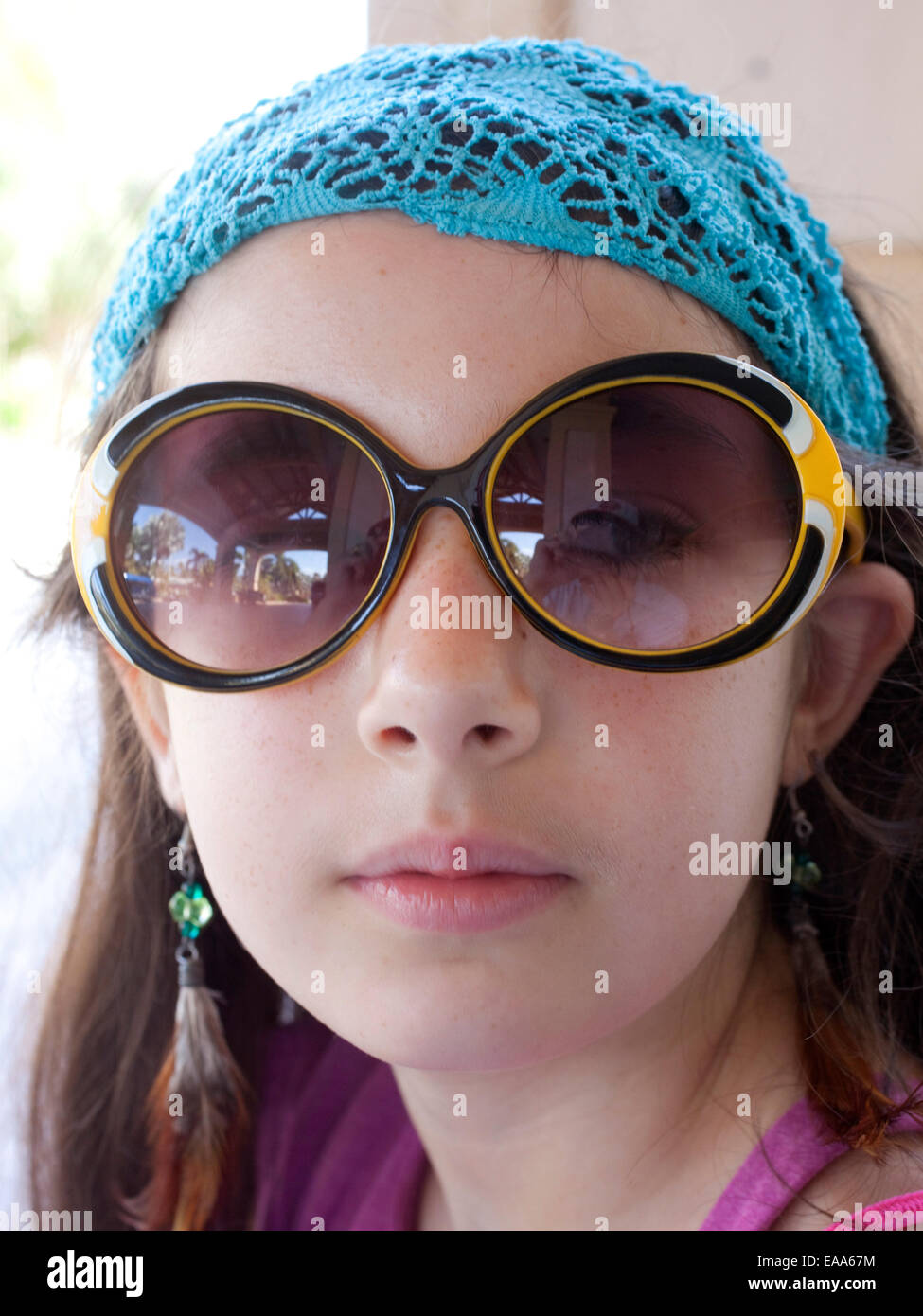 Ragazza giovane con occhiali da sole, orecchini in piuma e sciarpa di testa Foto Stock