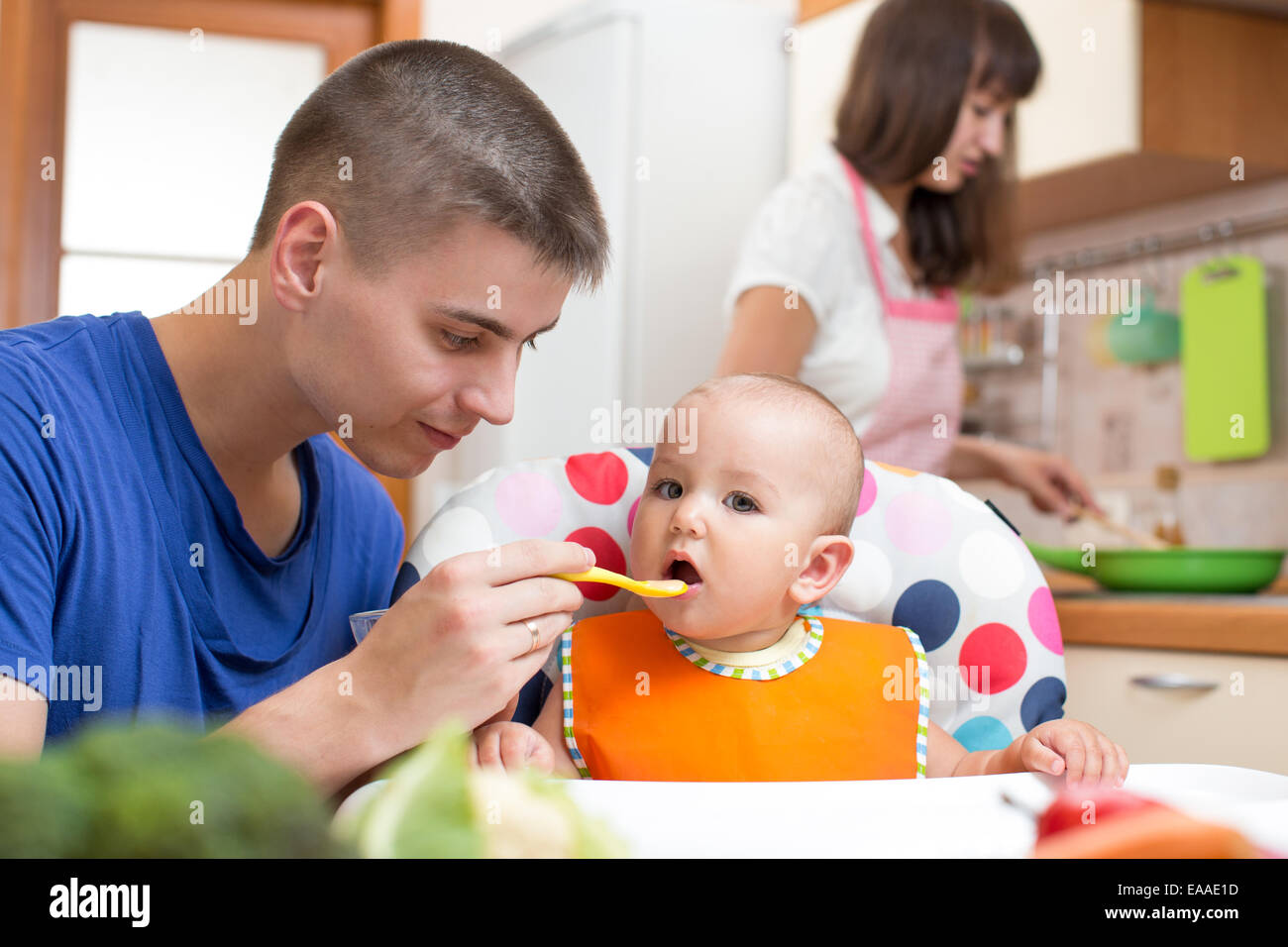 Padre alimentando il suo bambino e la madre la cottura in cucina Foto Stock