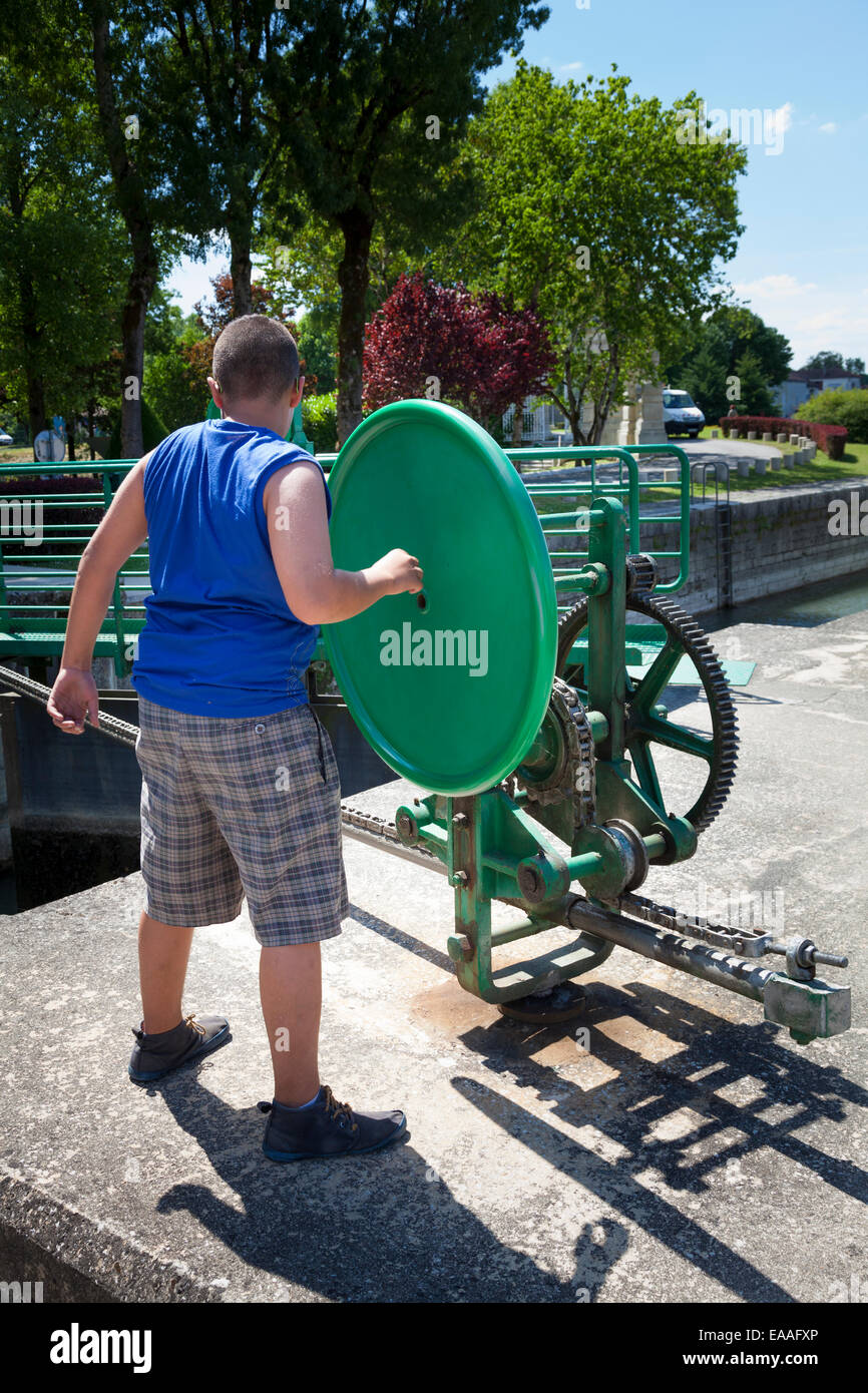 Un ragazzo azionando la serratura apertura cancello meccanismo ruota sul fiume Charente a Jarnac Foto Stock