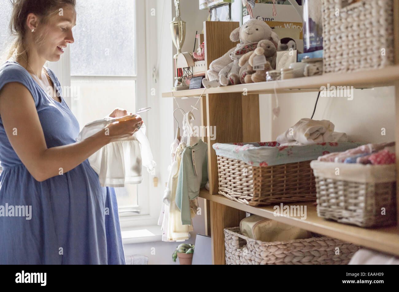 Una donna in stato di gravidanza in un vivaio di smistamento di vestiti del bambino. Foto Stock