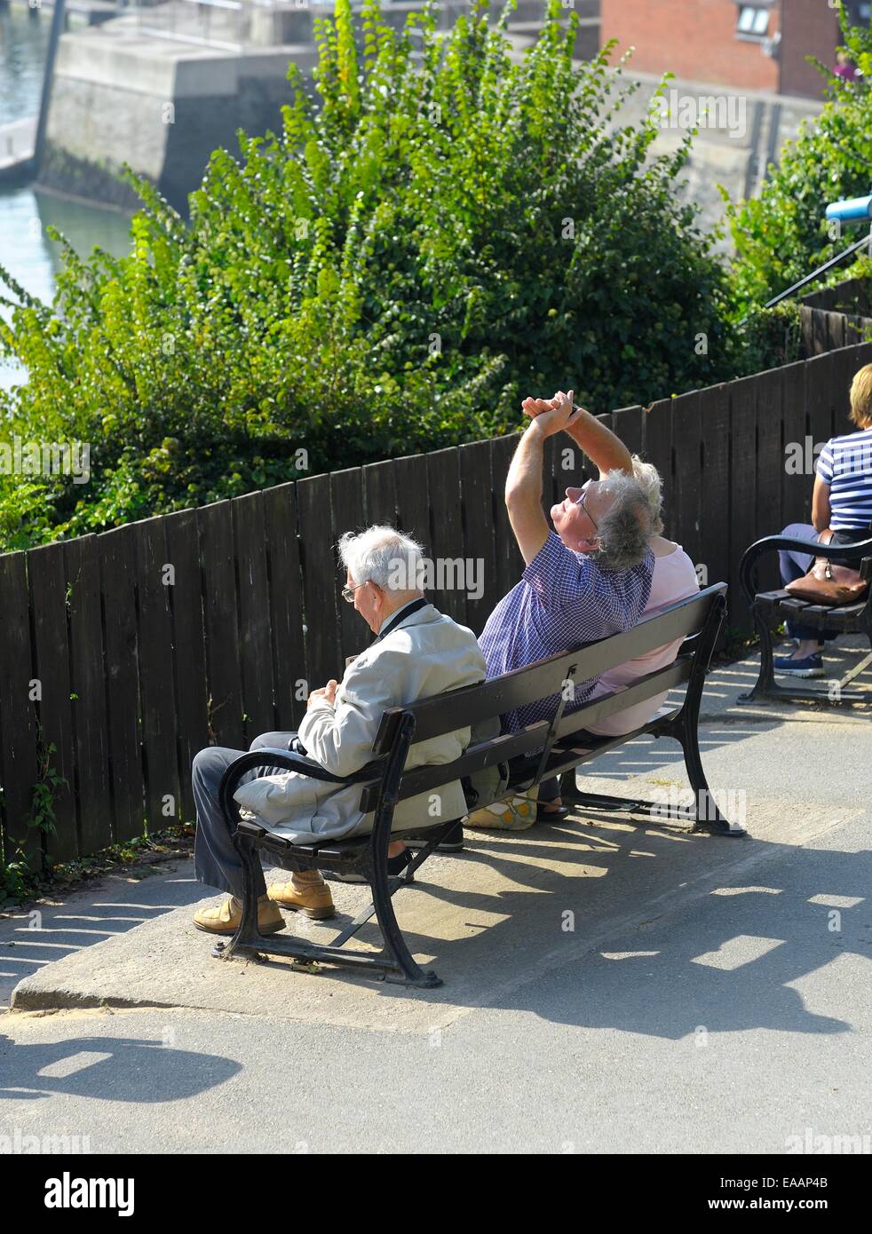 Un uomo con le sue mani a schermare gli occhi dal sole mentre seduta su una panchina, Padstow Cornwall Inghilterra Regno Unito Foto Stock