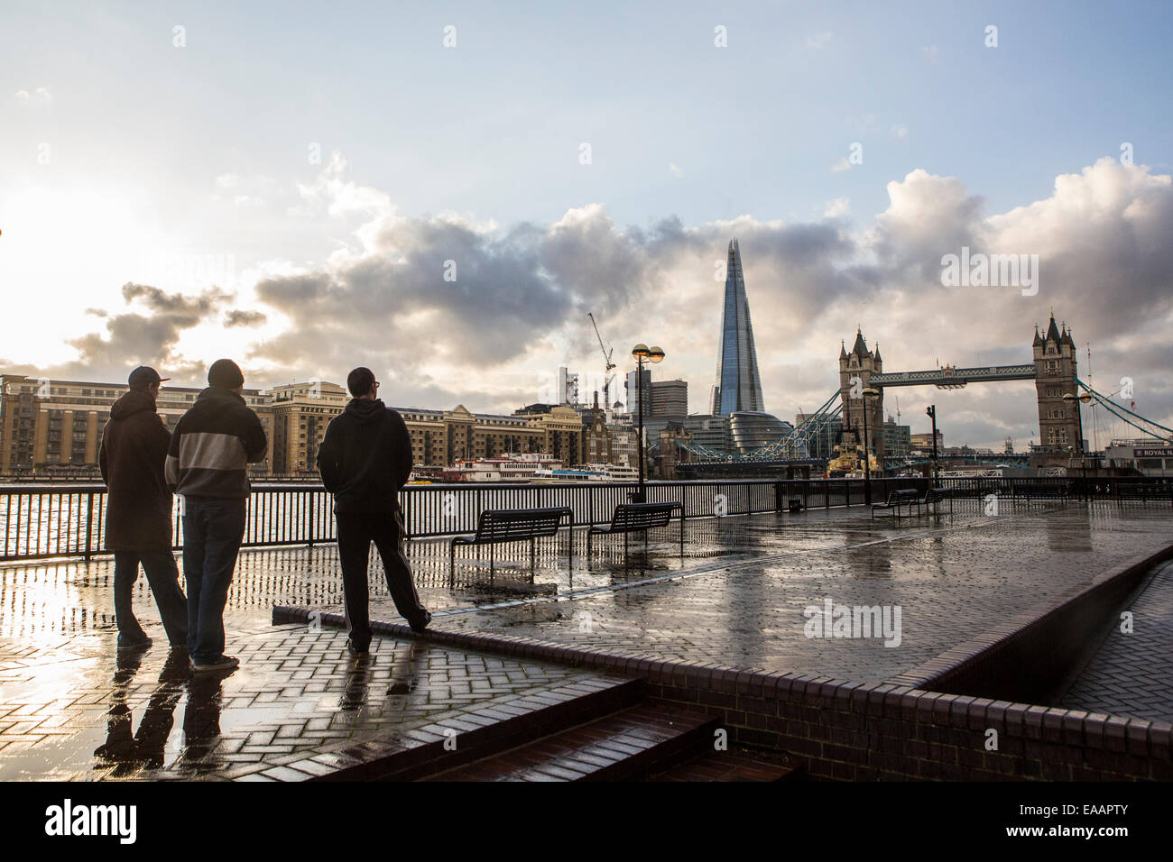 Tre giovani uomini si affacciano sul Fiume Tamigi per il Tower Bridge e la Shard a Londra dopo la pioggia. Foto Stock