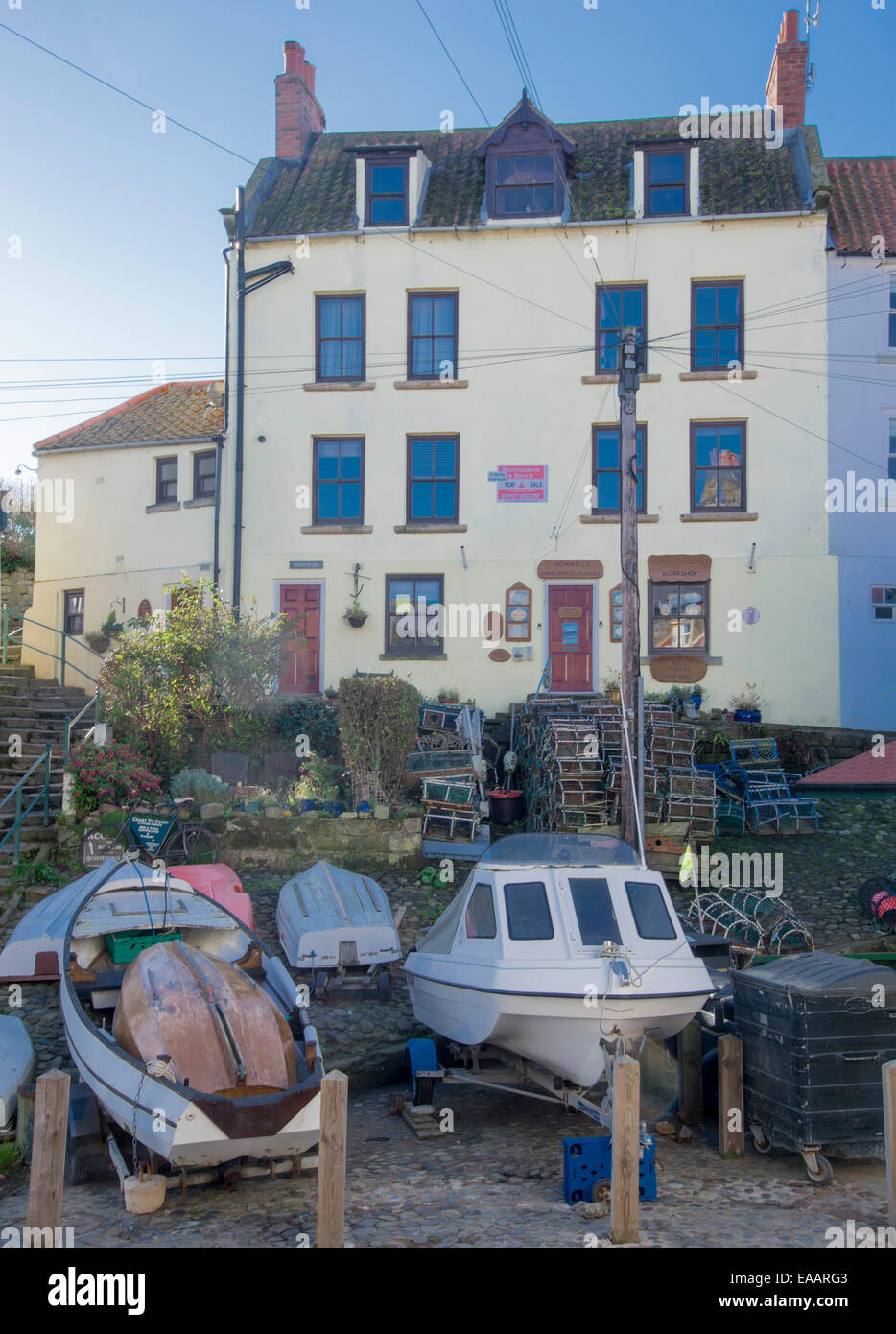 Giallo fiammante albergo/casa contro il cielo blu con barche e attrezzi da pesca in primo piano. Robin cappe Bay, North Yorkshire 2014 Foto Stock