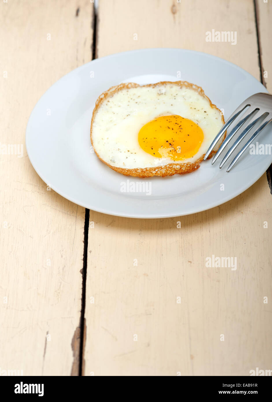 Uovo fritto soleggiato lato su una piastra con la forcella sulla tavola di legno Foto Stock