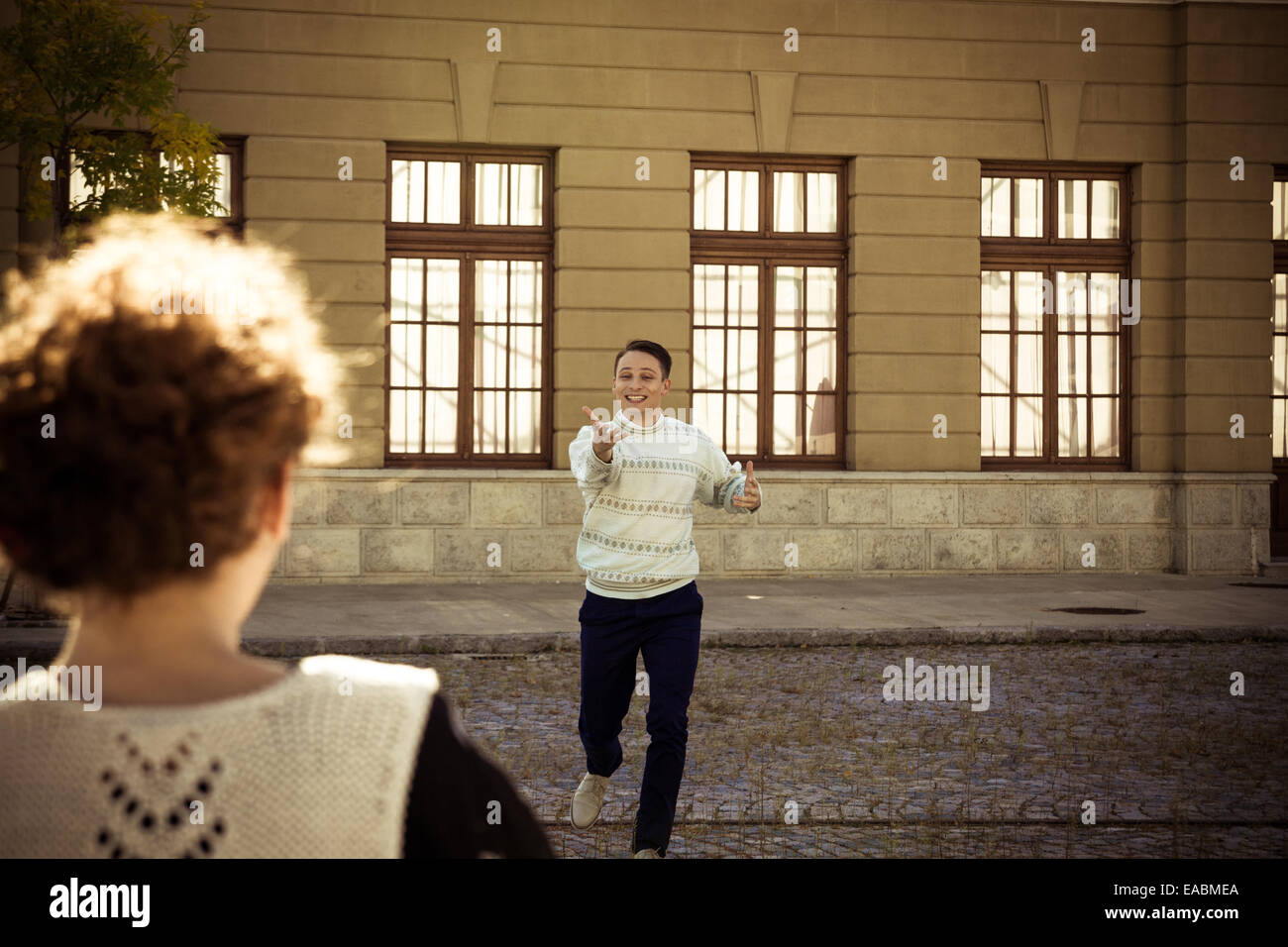 Ragazza posa sul banco mentre uomo sorridente in background sventolare di girare verso di lui e correre a lei, incontro o riunione di amici Foto Stock