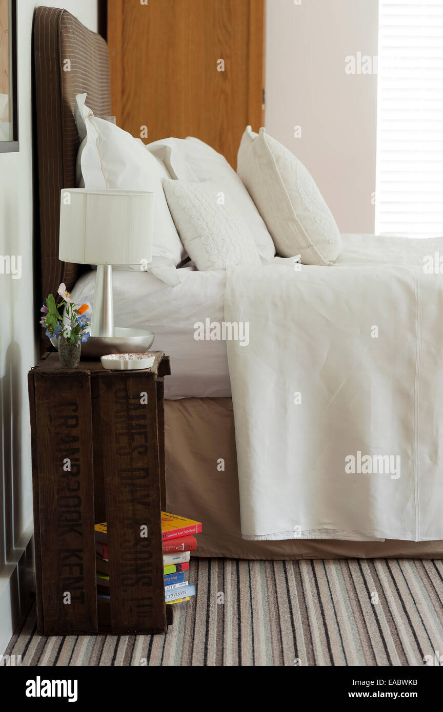 Vecchia cassa di apple utilizzato come comodino in camera da letto con lenzuola bianche e tappeti a strisce Foto Stock