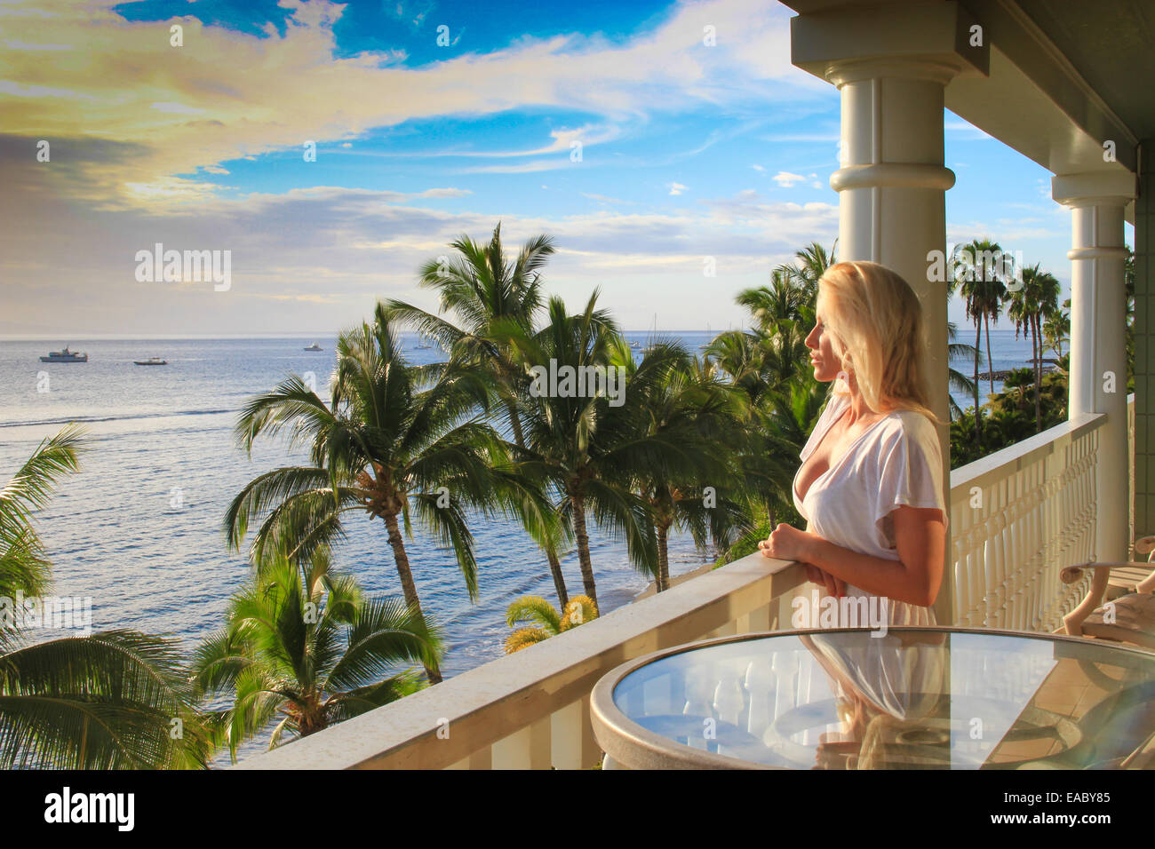 Attraente bionda signora in un ambiente tropicale che si affaccia sul bellissimo mare da un balcone Foto Stock