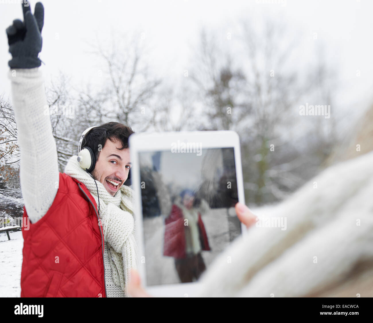 La donna a scattare foto di uomo con cuffie con computer tablet in inverno Foto Stock