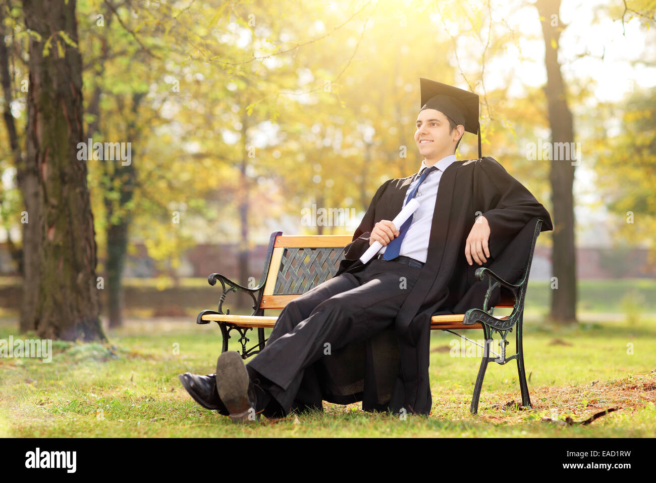 College Graduate godendo nel parco seduto su un banco di lavoro Foto Stock